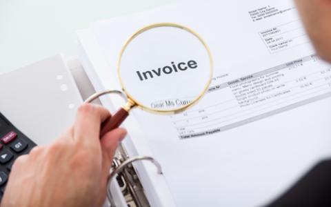 Professional using magnifying glass on Invoice report.