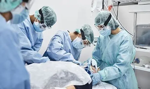 Team of doctors and nurses operating male patient in ICU. Frontline workers are treating man for coronavirus. They are in protective workwear.