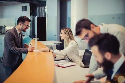 man signing a form at a receptionists desk