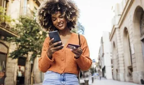 woman walking down the street with her smartphone and credit card in hand