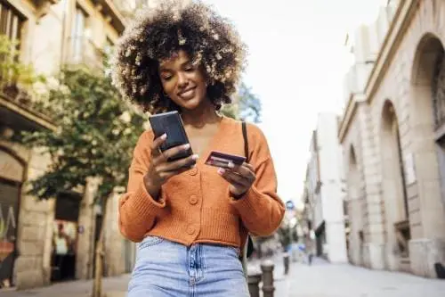 woman walking down the street with her smartphone and credit card in hand