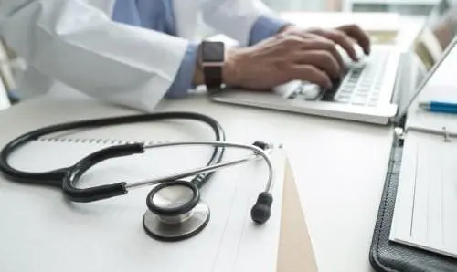 close up of stethoscope and medical professional typing on a keyboard