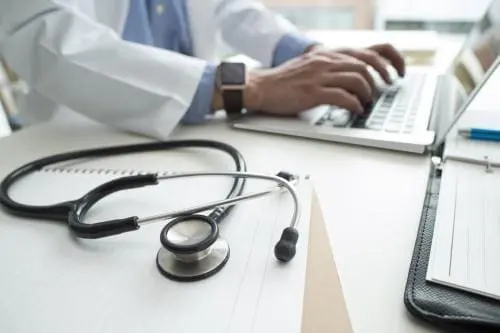 close up of stethoscope and medical professional typing on a keyboard