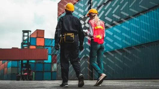 Image of two people in construction hats walking through an area with cargo shipping containers