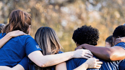 Image of a team huddled together with their arms around each other