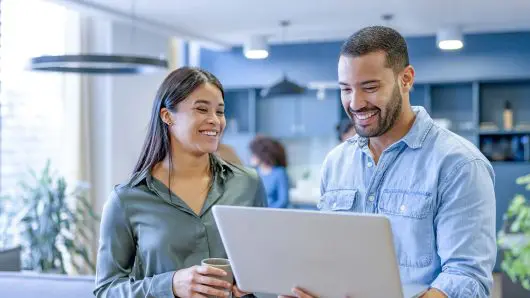 Two people working in an office setting looking at a laptop
