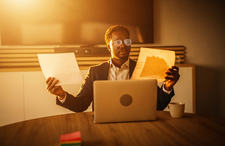 A man looking at two data sheets while sitting in front of his computer