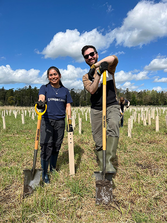 A female and male Coupa employee leans on their shovels under a blue sky