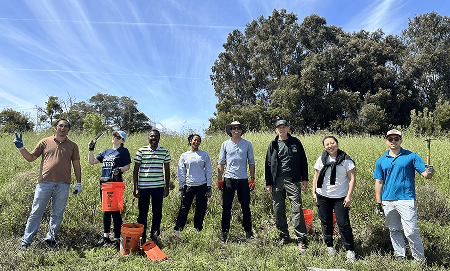 Coupa employees equipped with pickaxes, trowels, and utility buckets pose for a photo under a blue sunny sky