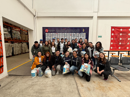 Coupa Employees holding bags of food pose in front of a Bancos De Alimentos sign